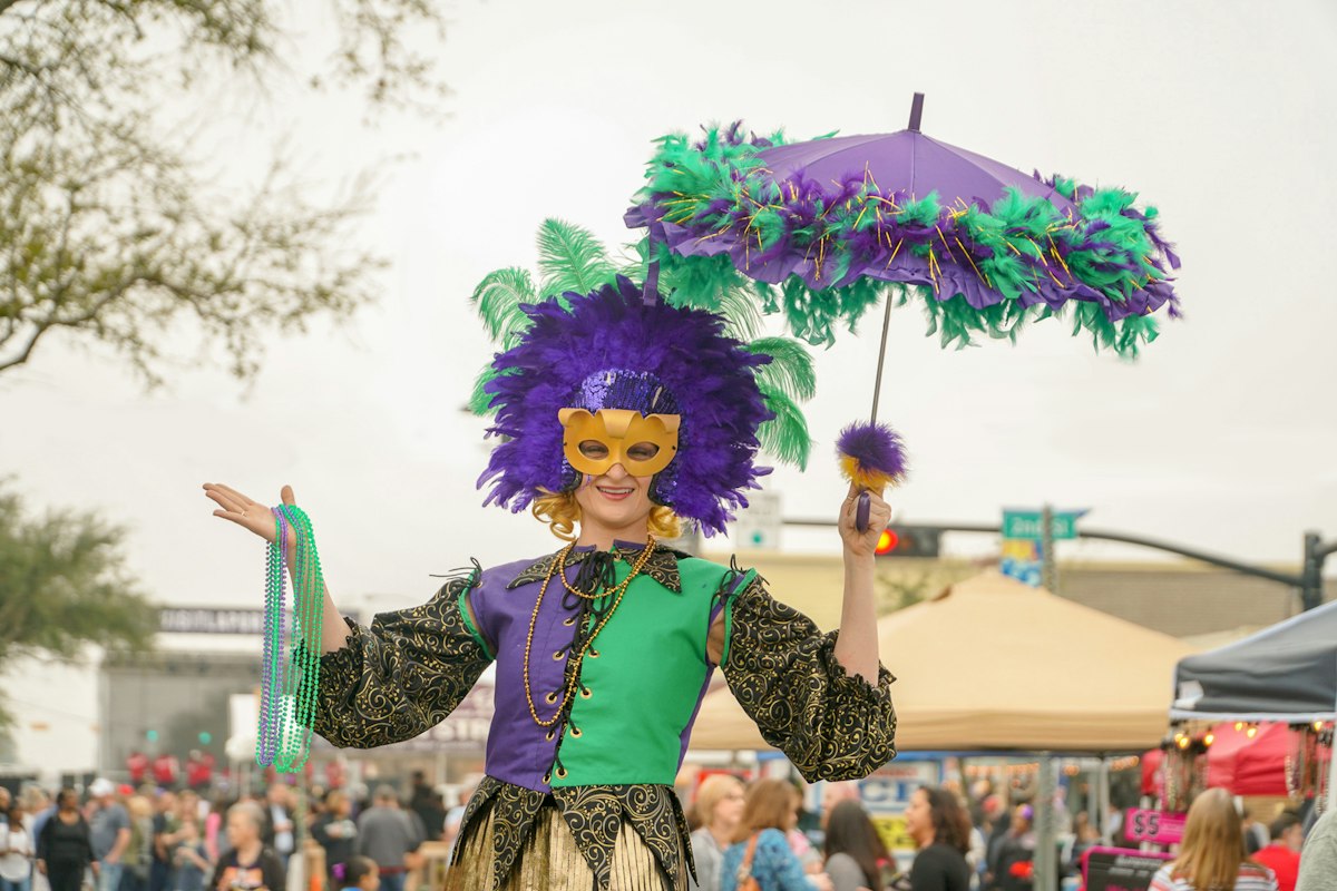 Person in a purple and green Mardi Gras costume holding a parasol