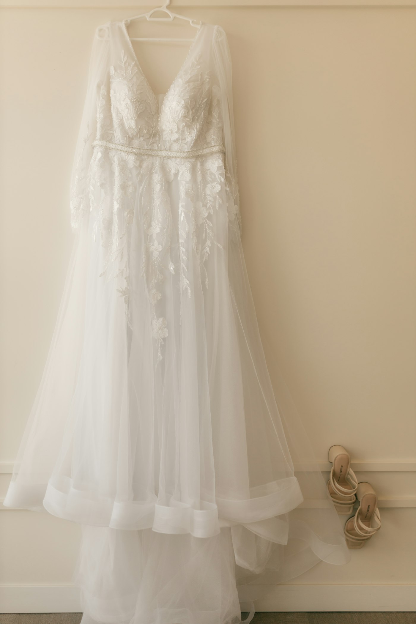 White wedding gown hanging beside a pair of shoes